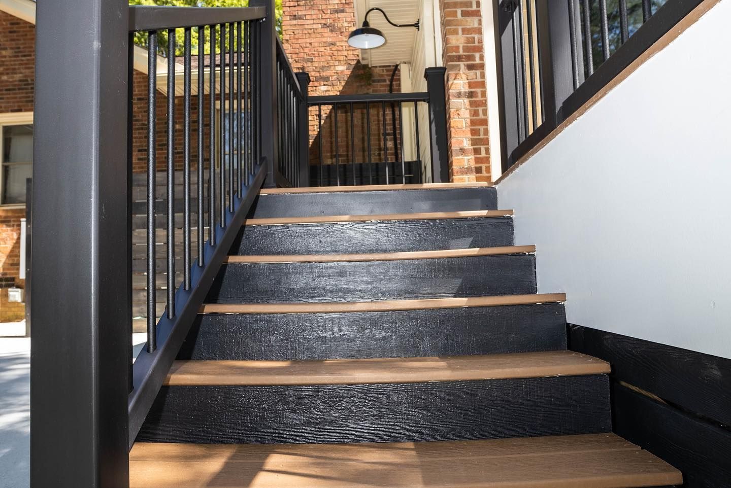 Black steps with wooden edges leading up a narrow outdoor staircase with black railings.