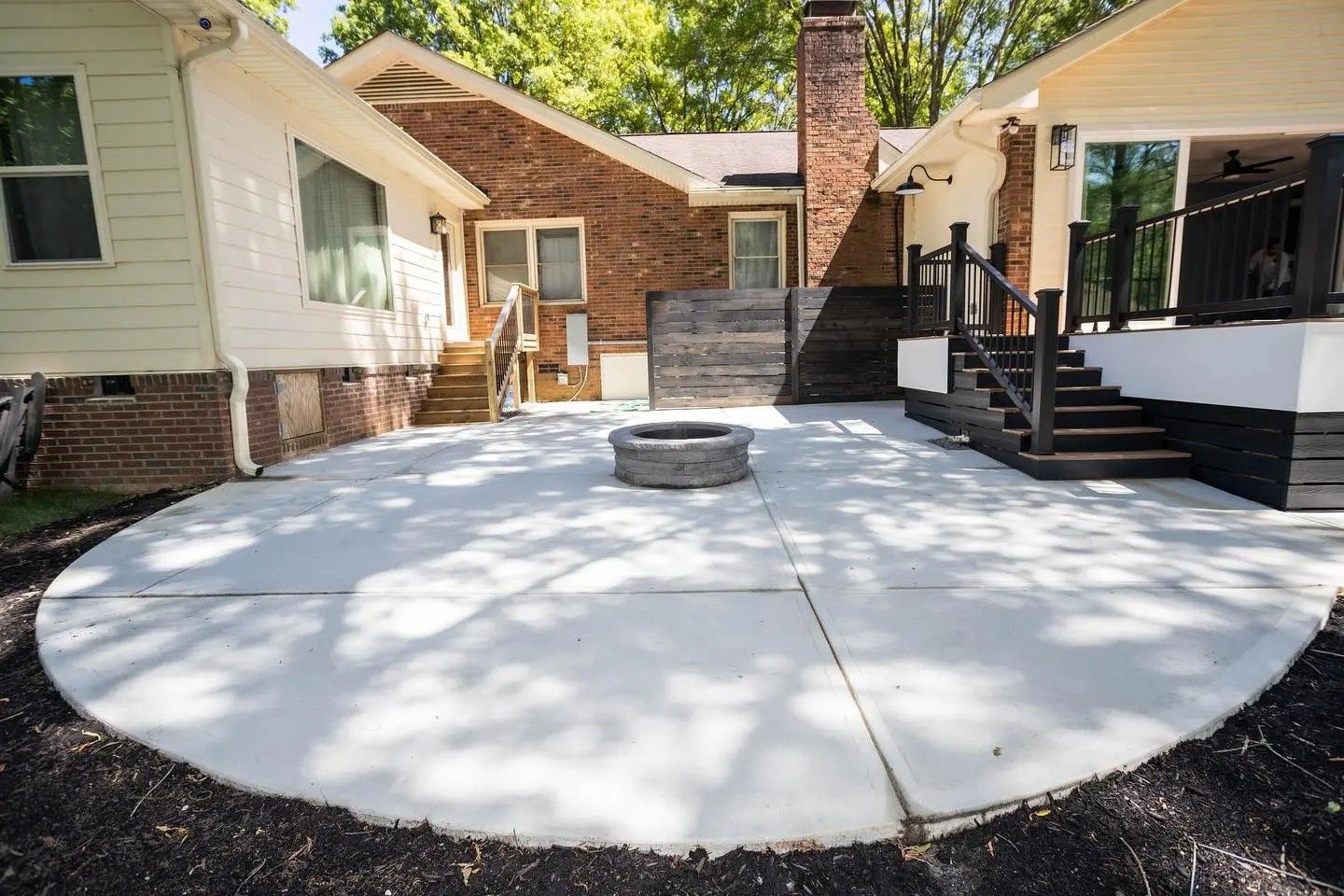 Backyard concrete patio with a circular fire pit and steps leading to a porch.