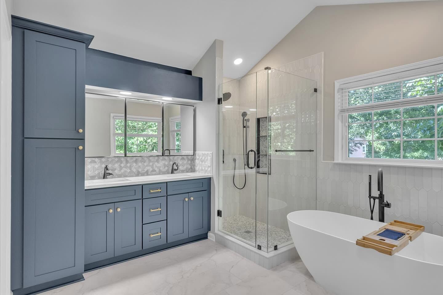 Blue bathroom vanity with mirror, glass shower, and freestanding tub in a bright modern space