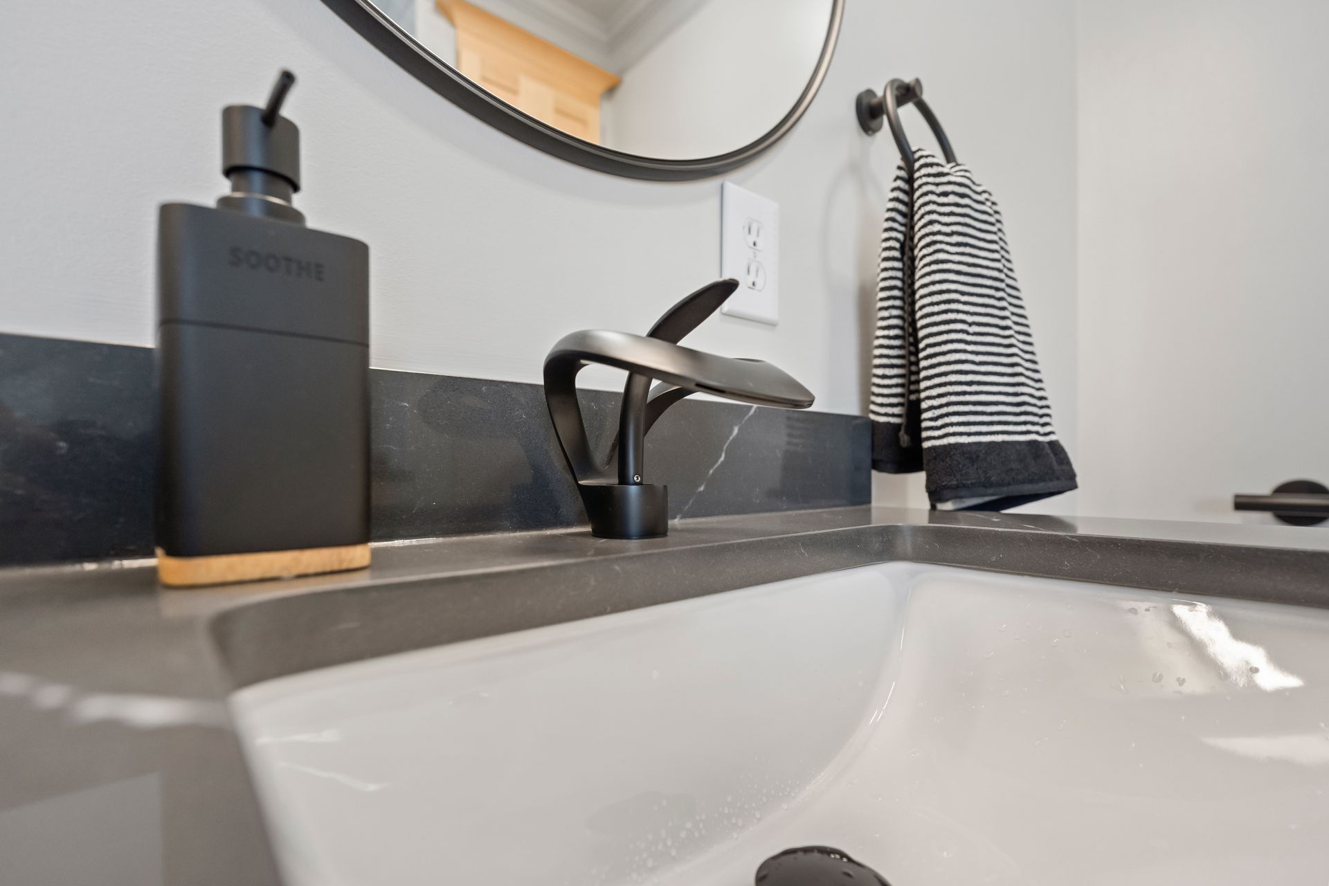 Modern bathroom sink with black faucet, soap dispenser, and striped hand towel on a gray countertop.