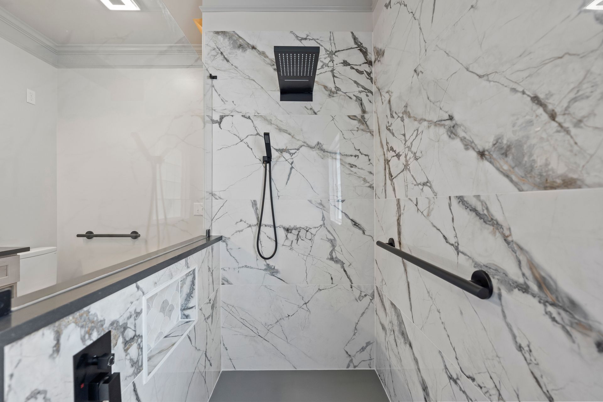 Modern marble-tiled walk-in shower with black fixtures, glass panel, and handheld showerhead