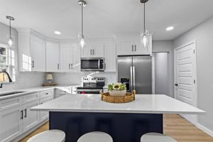 Bright white modern kitchen with island, stainless steel appliances, and pendant lights