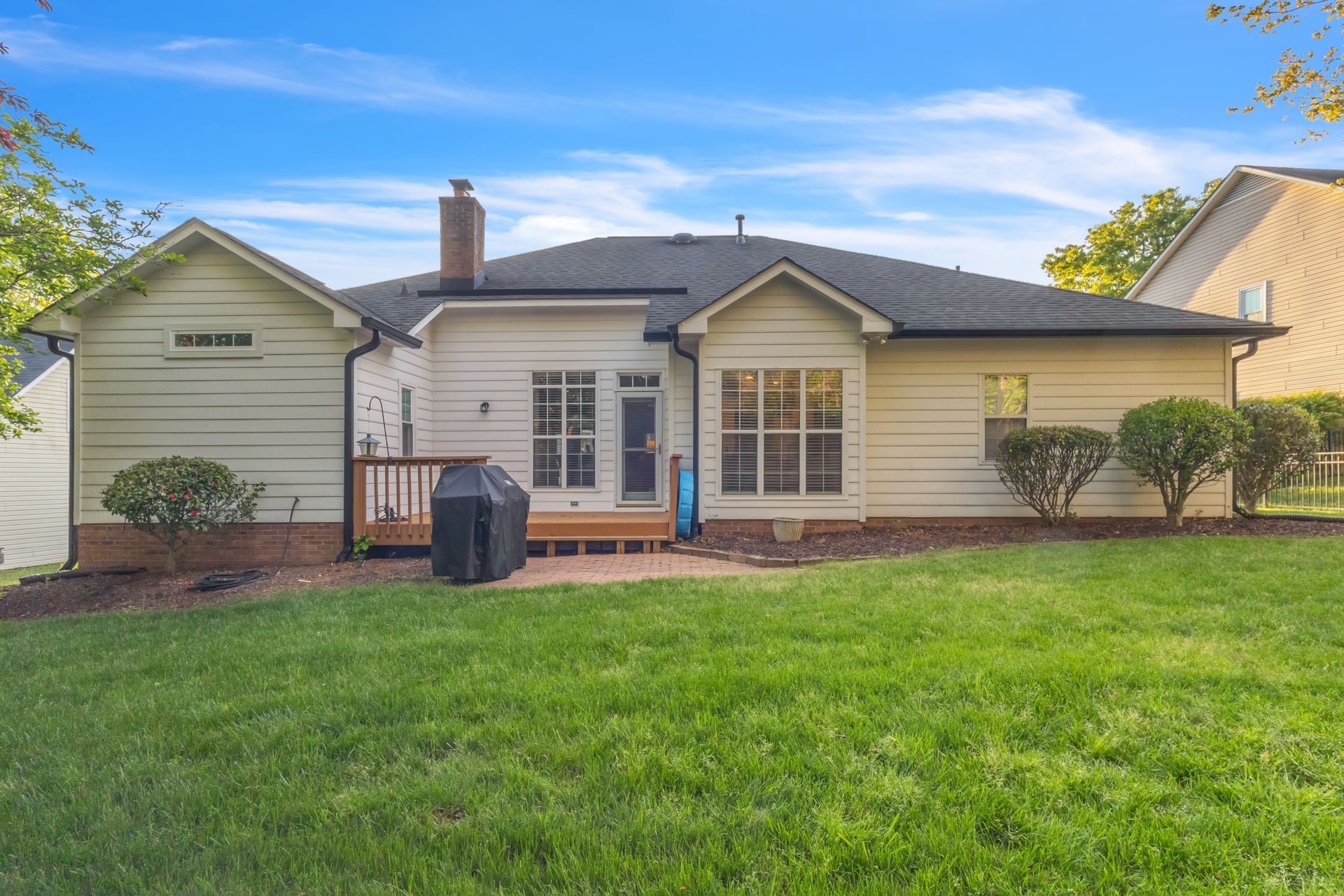 Single-story suburban house with a front lawn, brick walkway, and blue sky above