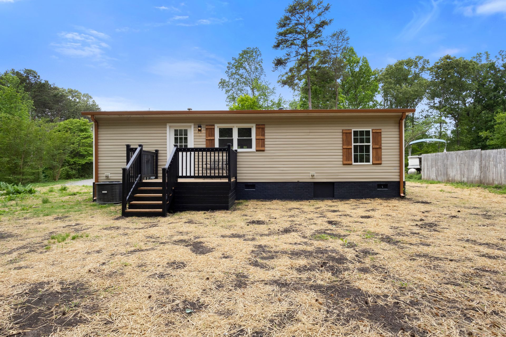 Single-story beige house with a small black front deck in a grassy yard under a blue sky