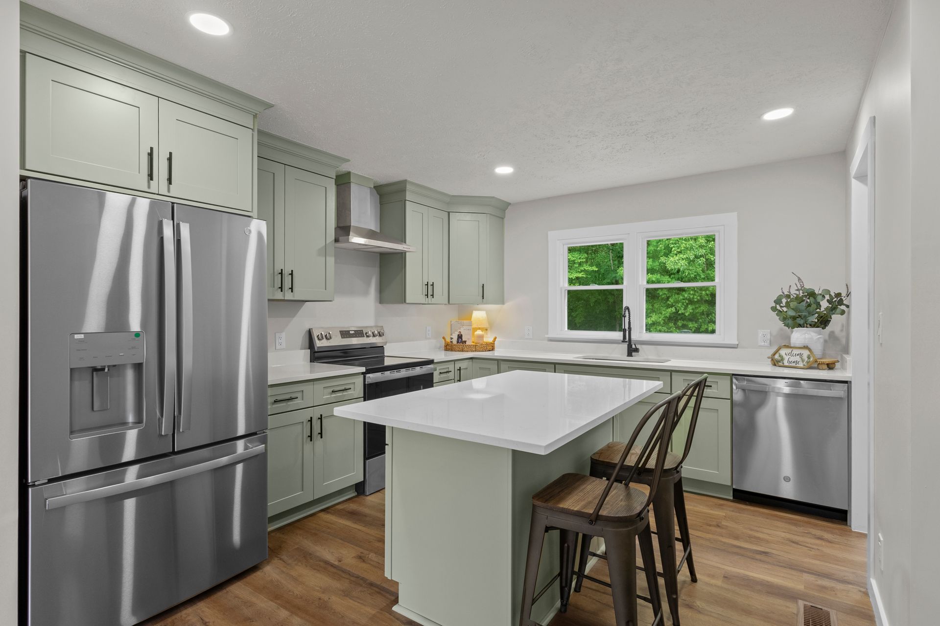 Bright modern kitchen with stainless steel appliances, white cabinets, island, and large window.
