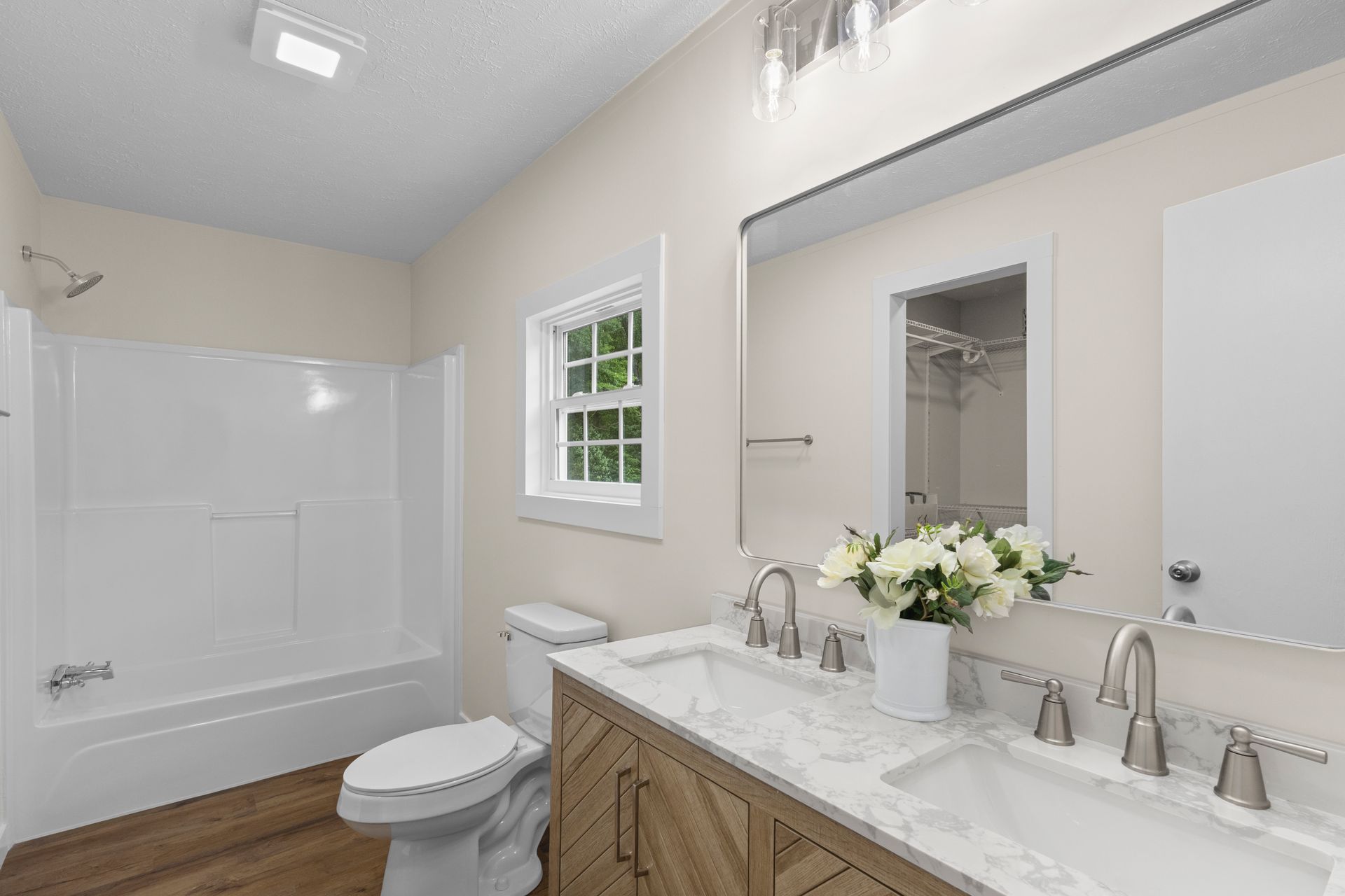 Bright bathroom with white tub, window, and vanity with mirror and flowers