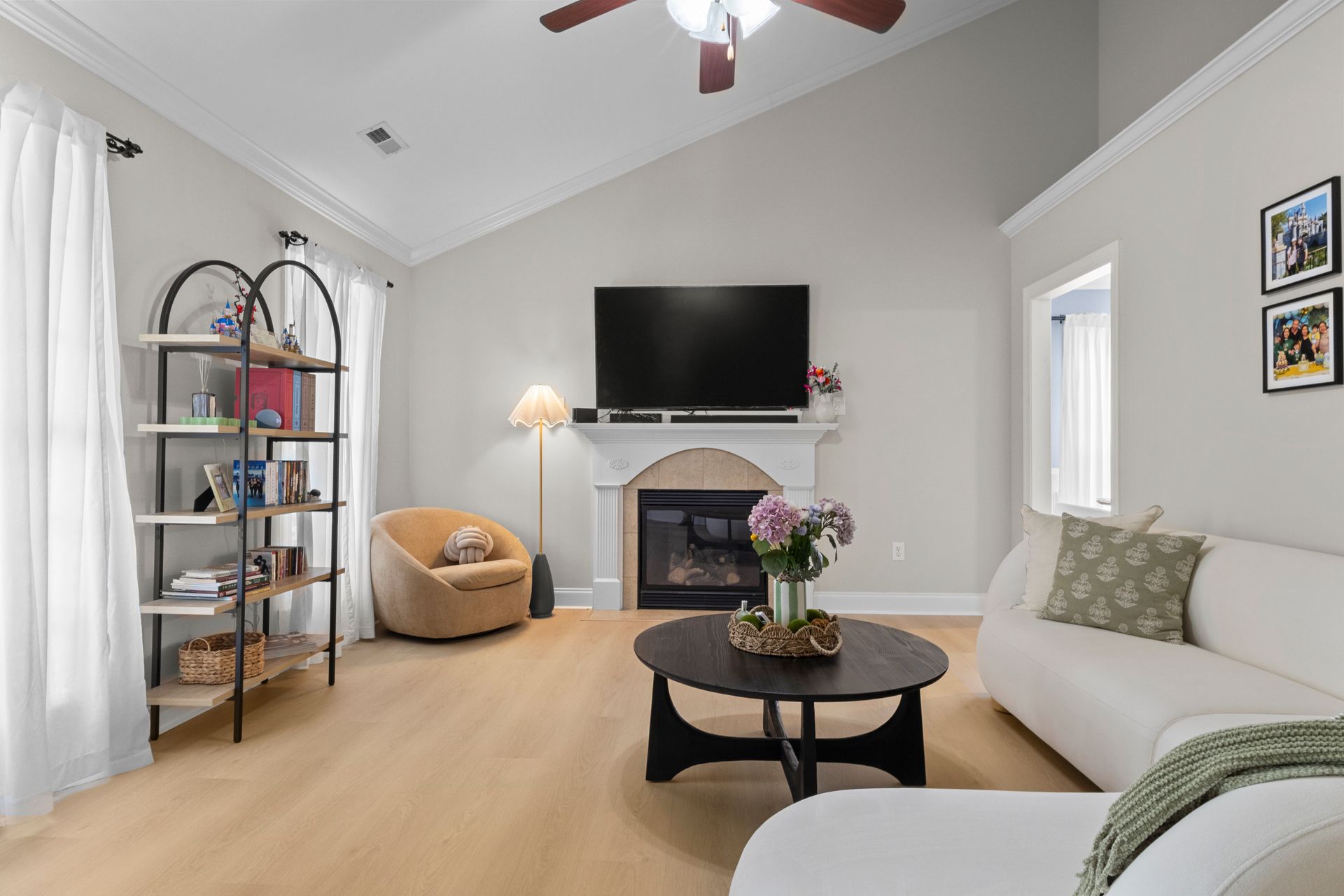 Bright living room with white sofa, fireplace, wall TV, and wicker chair under vaulted ceiling.