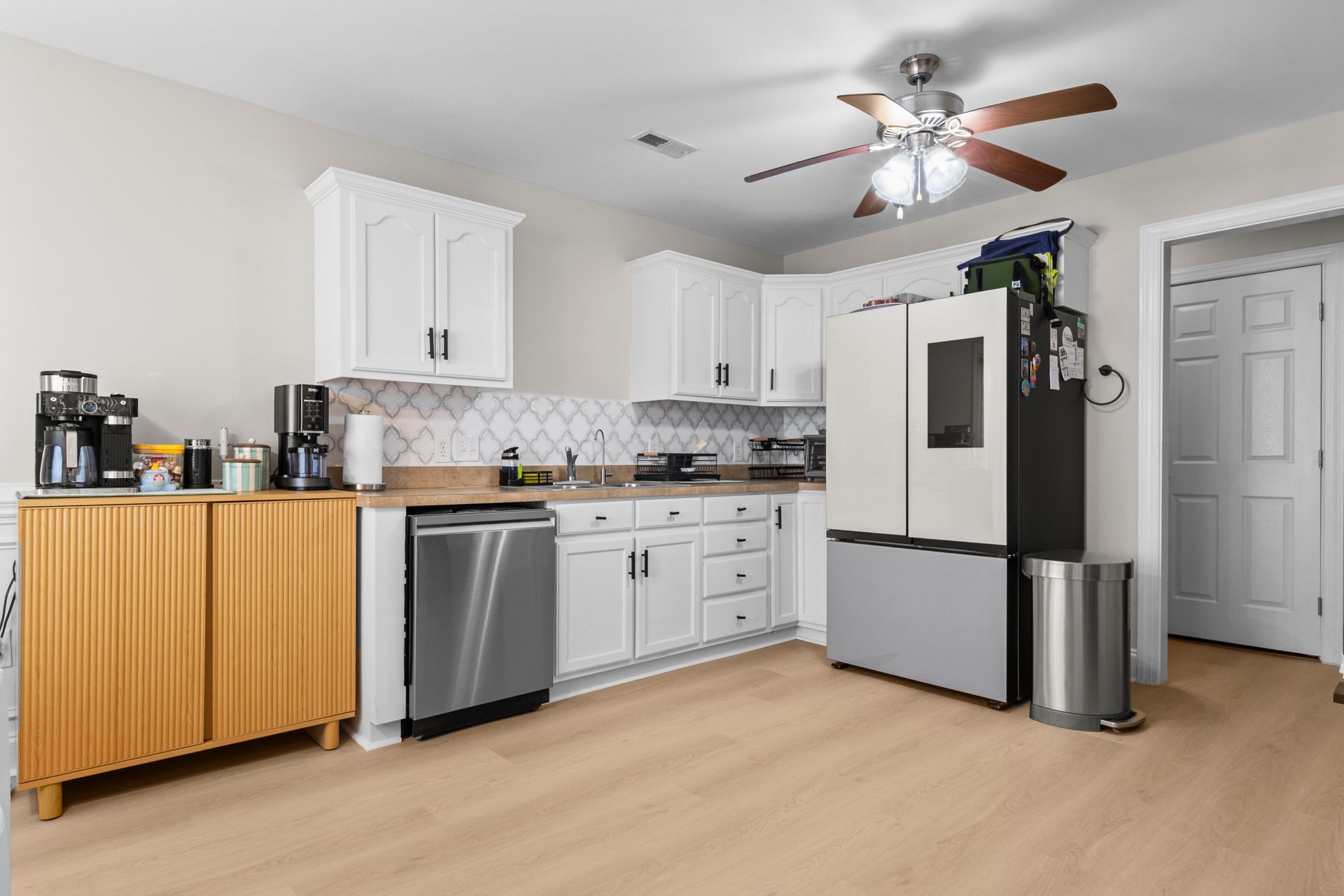 Modern kitchen with white cabinets, stainless appliances, wood floor, and ceiling fan