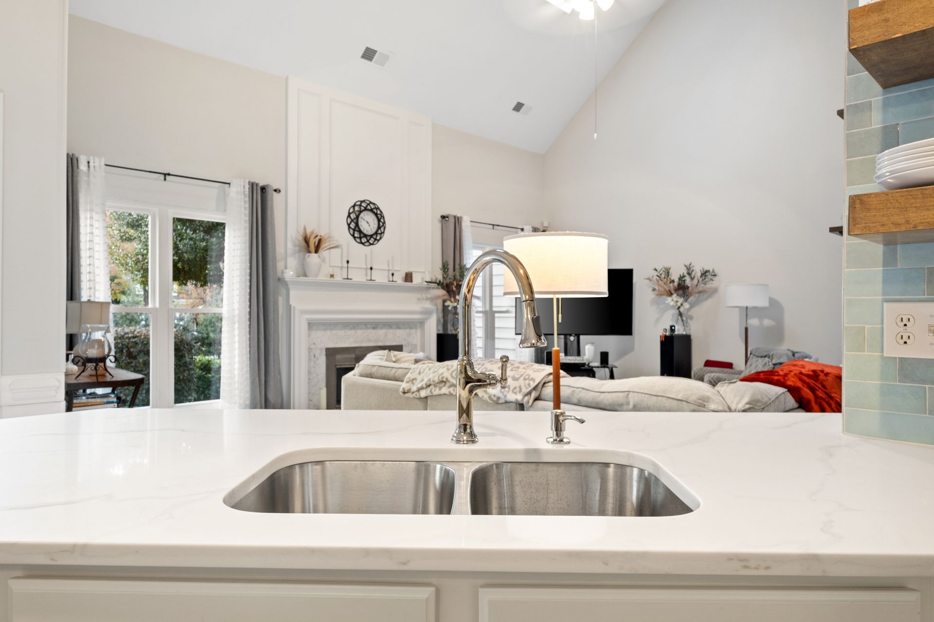 Bright modern kitchen with white island, stainless sink, and view into a living room with fireplace and sofa