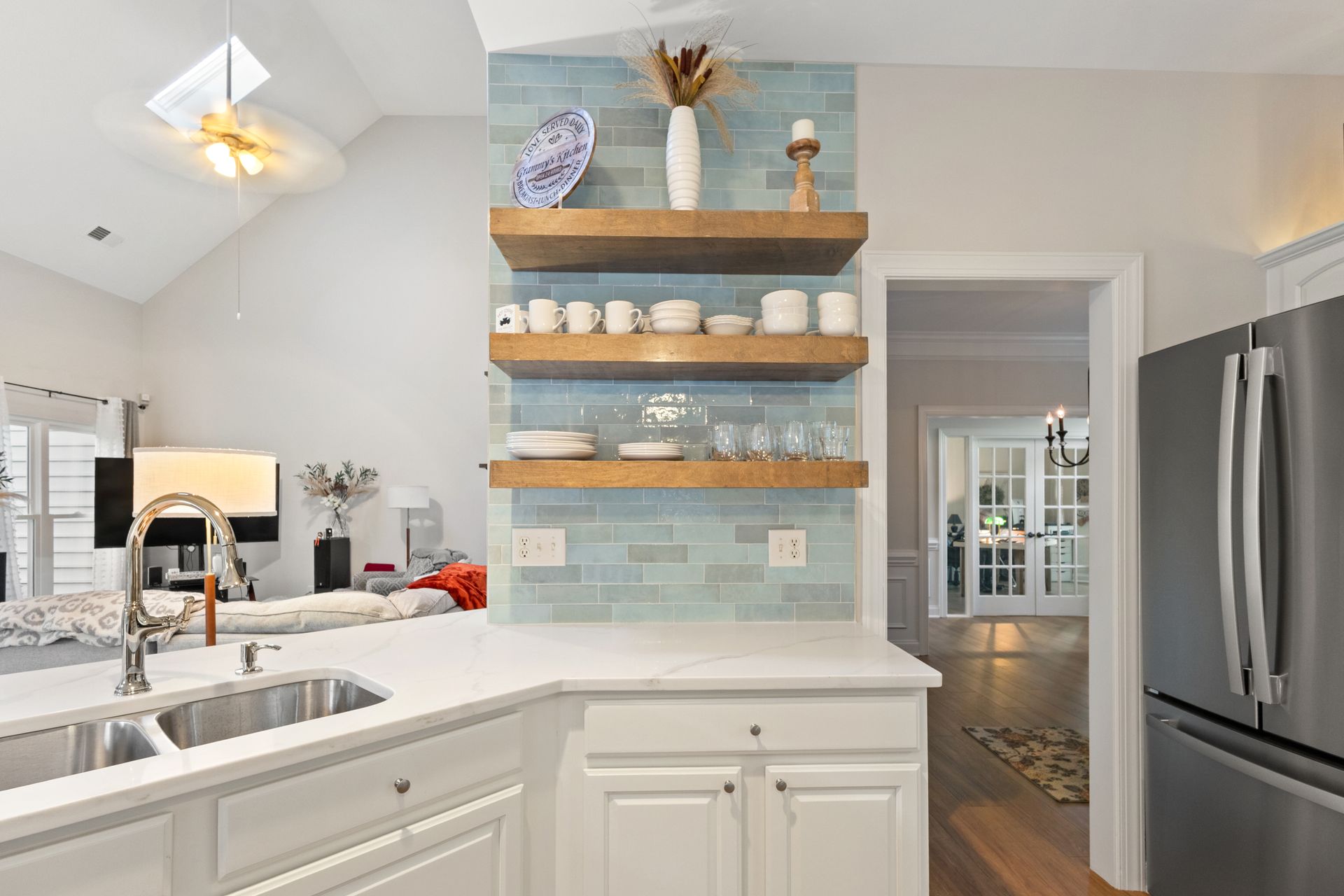 Bright modern kitchen with white cabinets, stainless fridge, blue tile backsplash, and open shelves