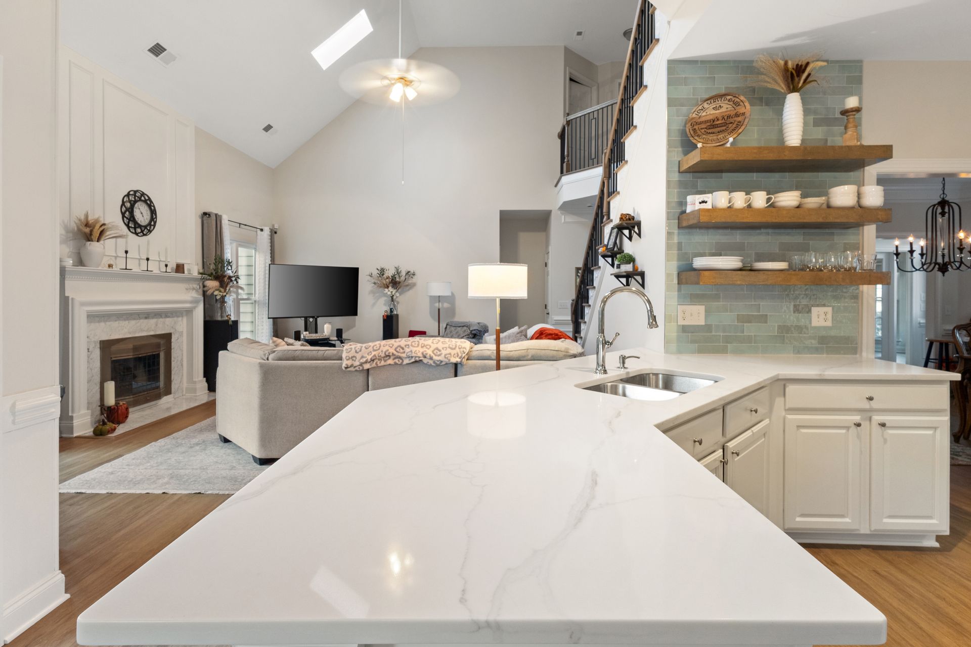 Bright modern kitchen open to living room with white island, fireplace, TV, and floating shelves