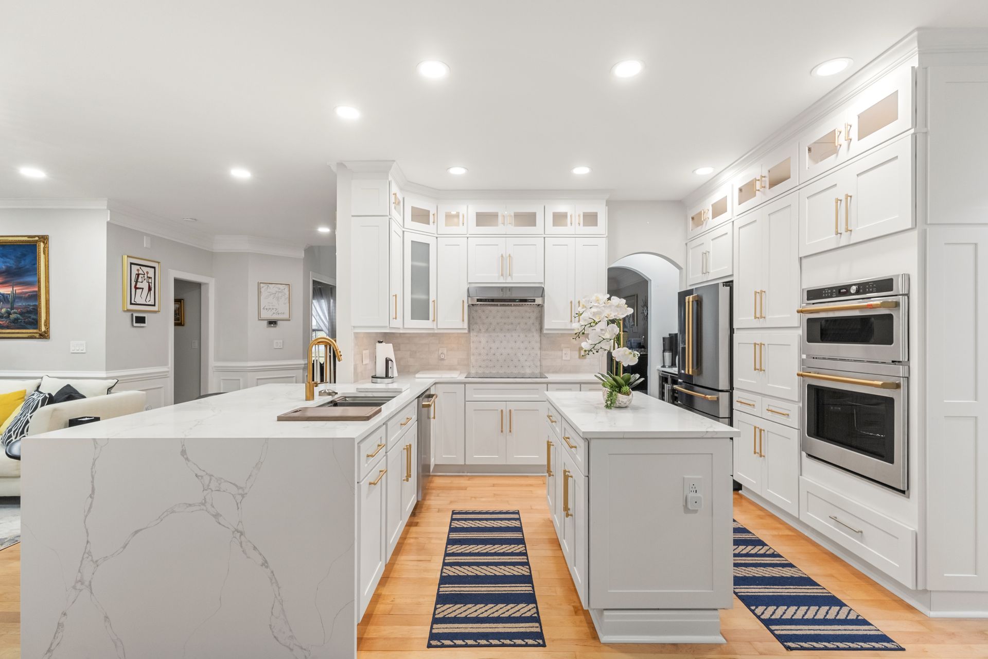 Bright white modern kitchen with island, built-in ovens, wood floor, and blue striped runners