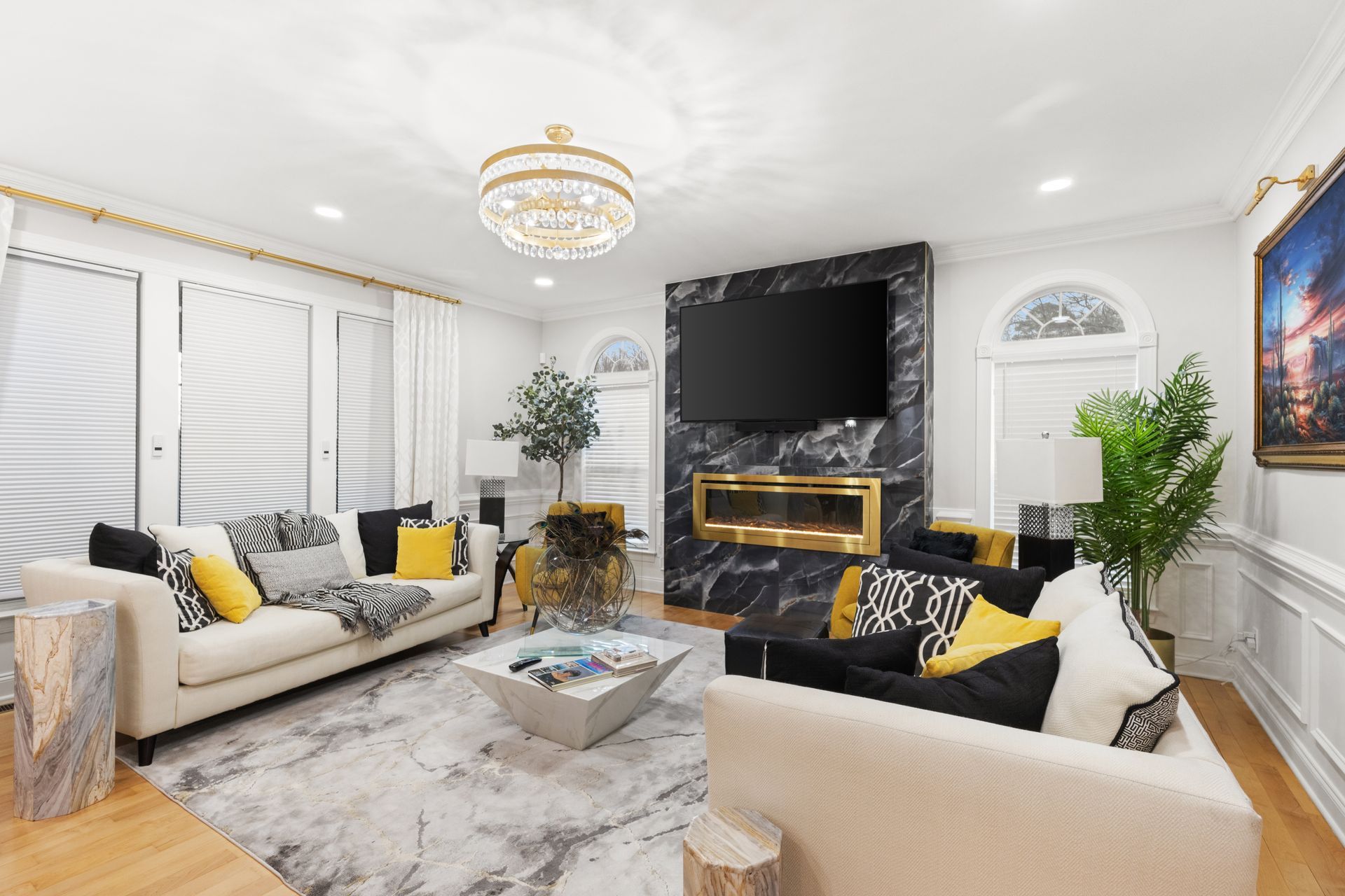 Bright living room with white sofas, black accents, chandelier, marble fireplace, and large TV