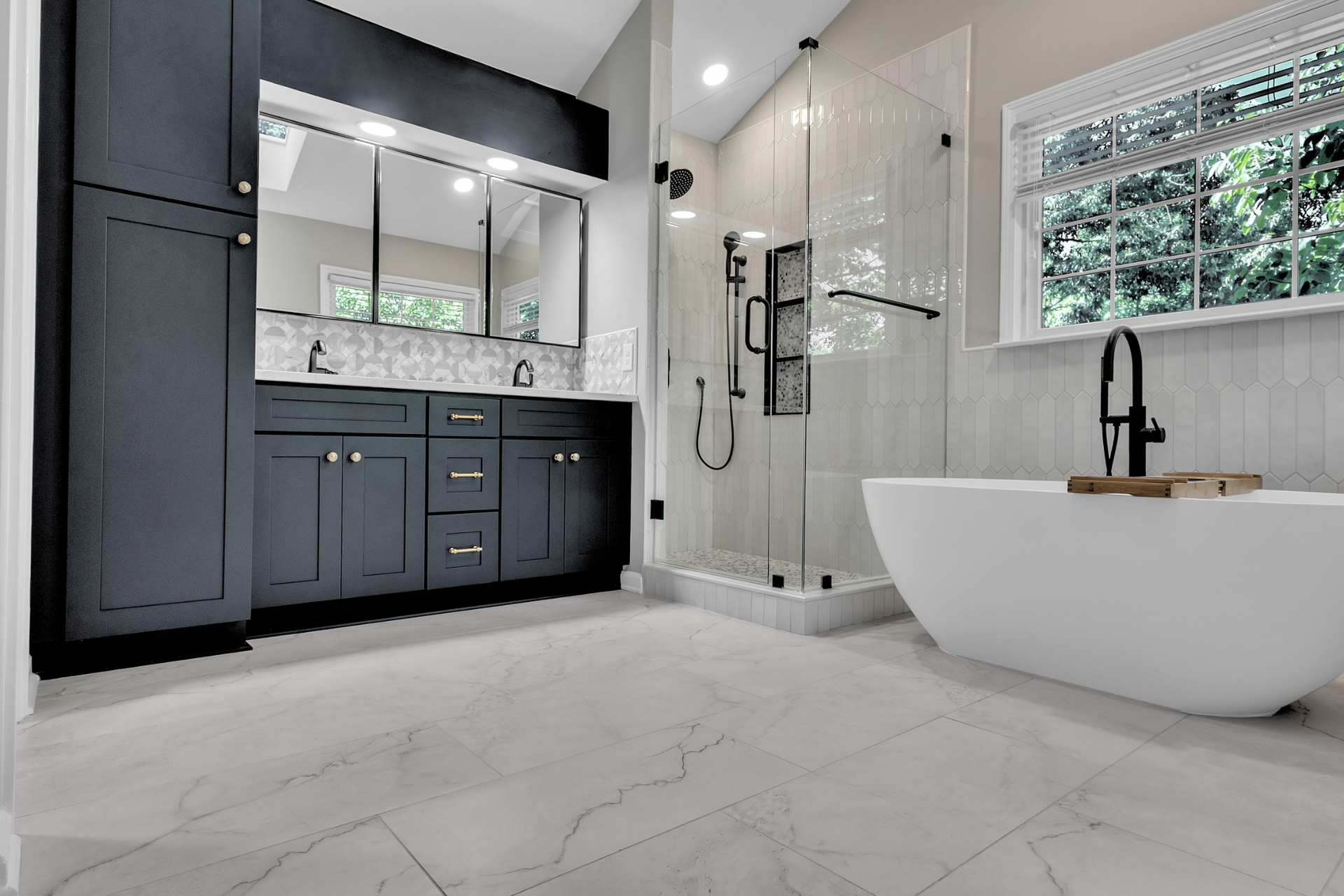 Modern bathroom with dark vanity, glass shower, freestanding tub, and large window