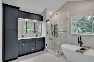 Modern bathroom with dark vanity, glass shower, and freestanding tub by a window