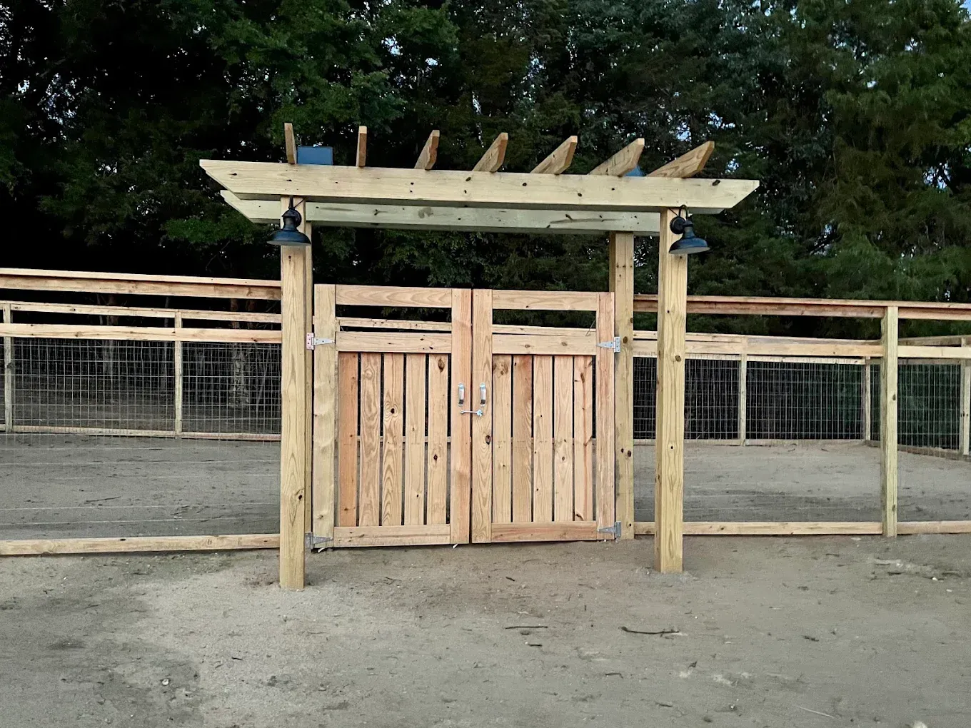 Wooden gate and pergola at an outdoor animal enclosure, with fenced sides and gravel ground.