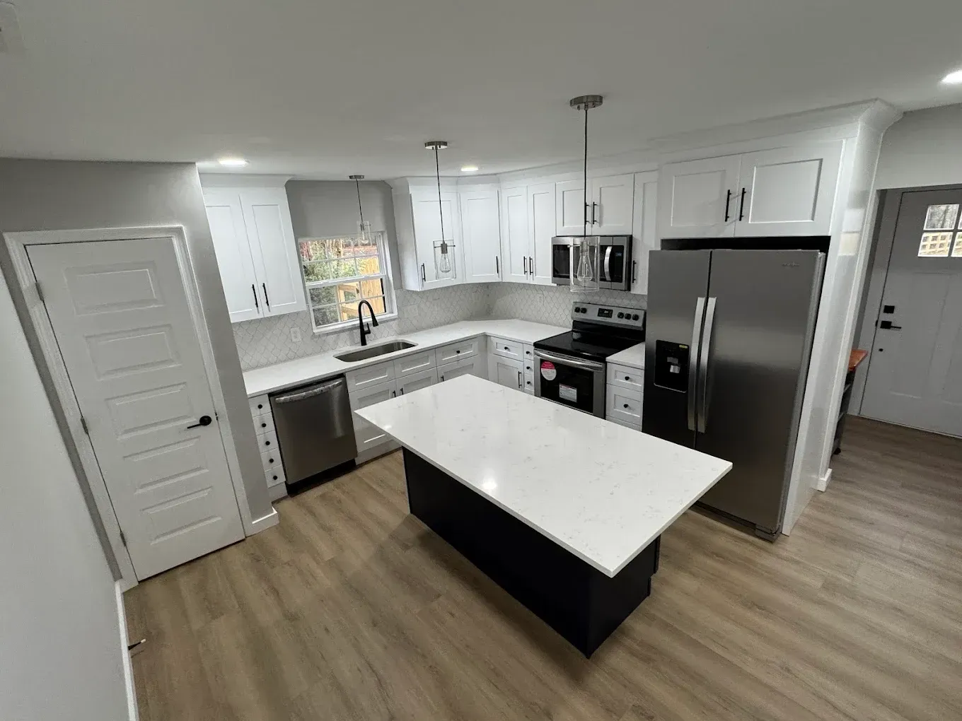 Bright modern kitchen with white cabinets, stainless appliances, and a large island with white countertop.
