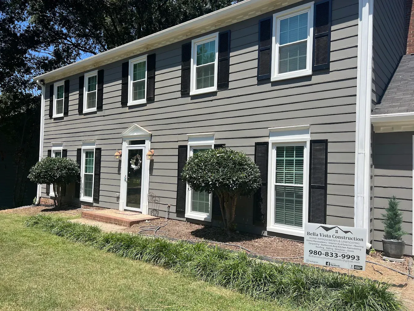 Two-story gray townhouse with white trim, shutters, and front lawn in sunlight