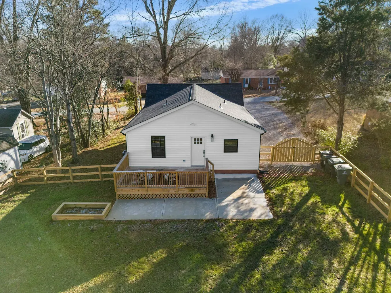 Small white house with a wooden deck, railing, and ramp beside a concrete patio in a grassy yard.