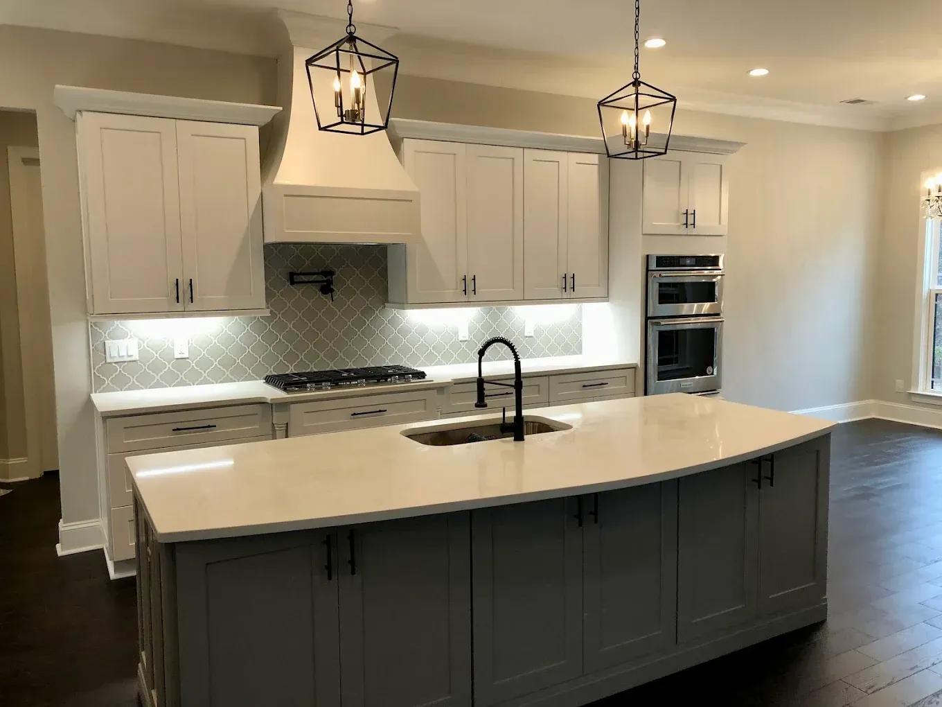 Modern kitchen with dark island, white cabinets, pendant lights, and stainless steel appliances