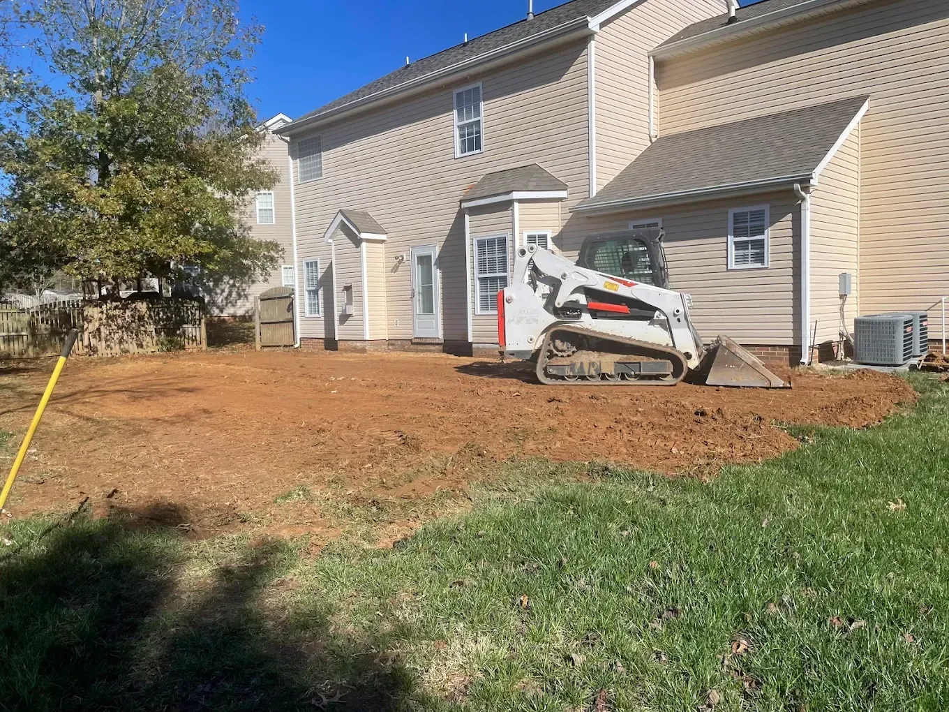 White stucco house with tan roof, fresh mulch, and a skid steer parked by the front door