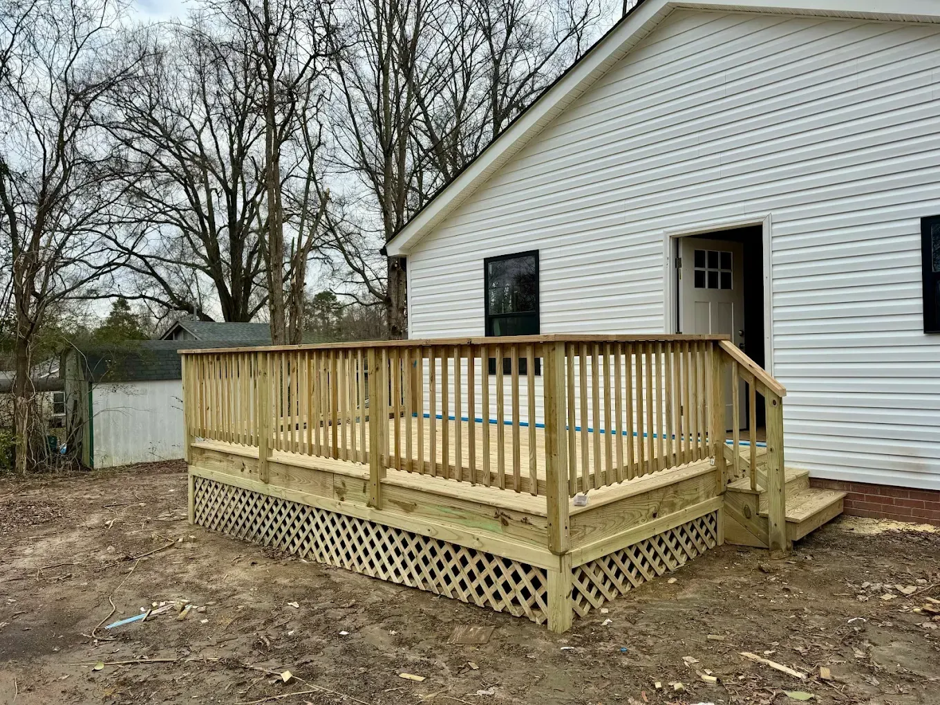 Wooden accessibility ramp with railing beside a white house on a bare yard