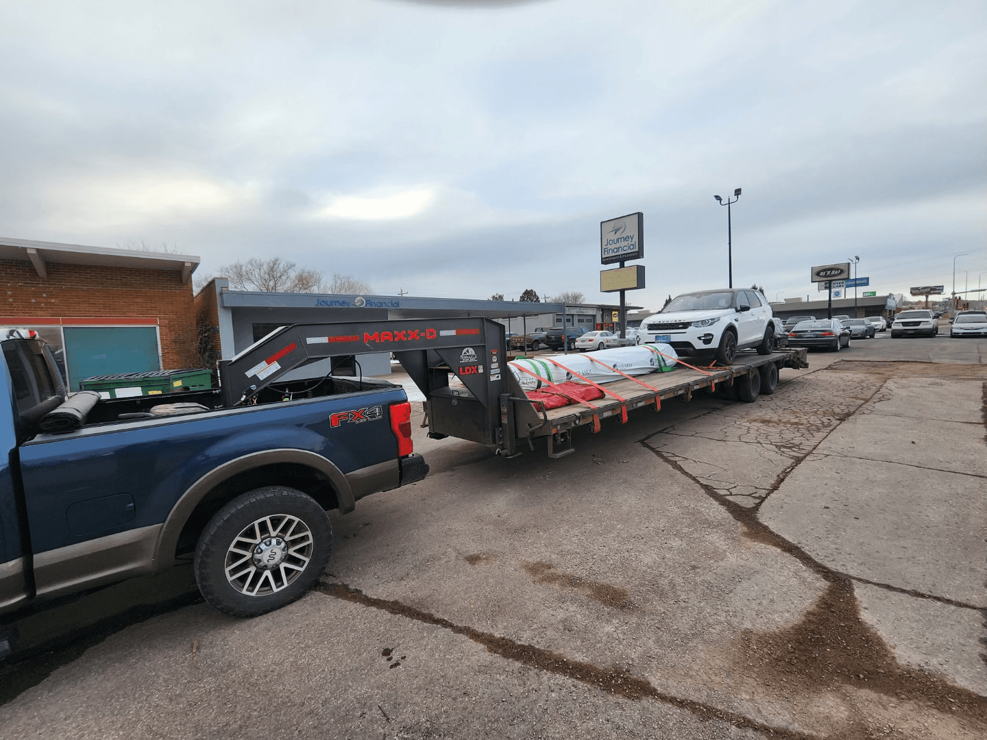 vehicle on a flatbed trailer with other tarping equipment being transported by a pickup truck 