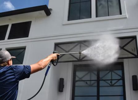 Man pressure washing white building facade with a water spray.