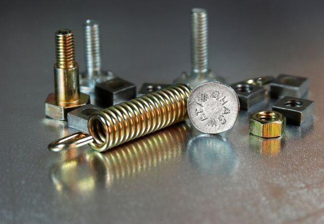 Vari tipi di viti, bulloni e molle metalliche sono sparsi su una superficie riflettente.
