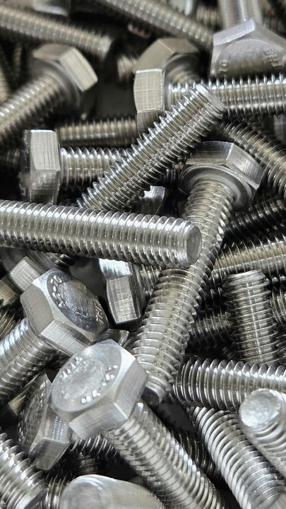 Un mucchio di bulloni e dadi in metallo argentato, impilati uno accanto all'altro.