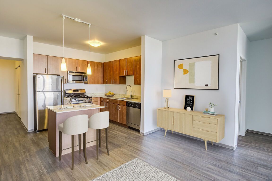 A kitchen with stainless steel appliances and wooden cabinets in a living room.