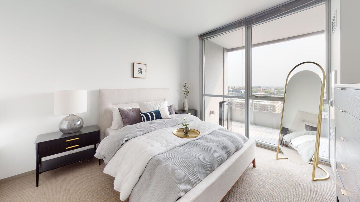 A bedroom with a bed , nightstand , mirror and balcony.