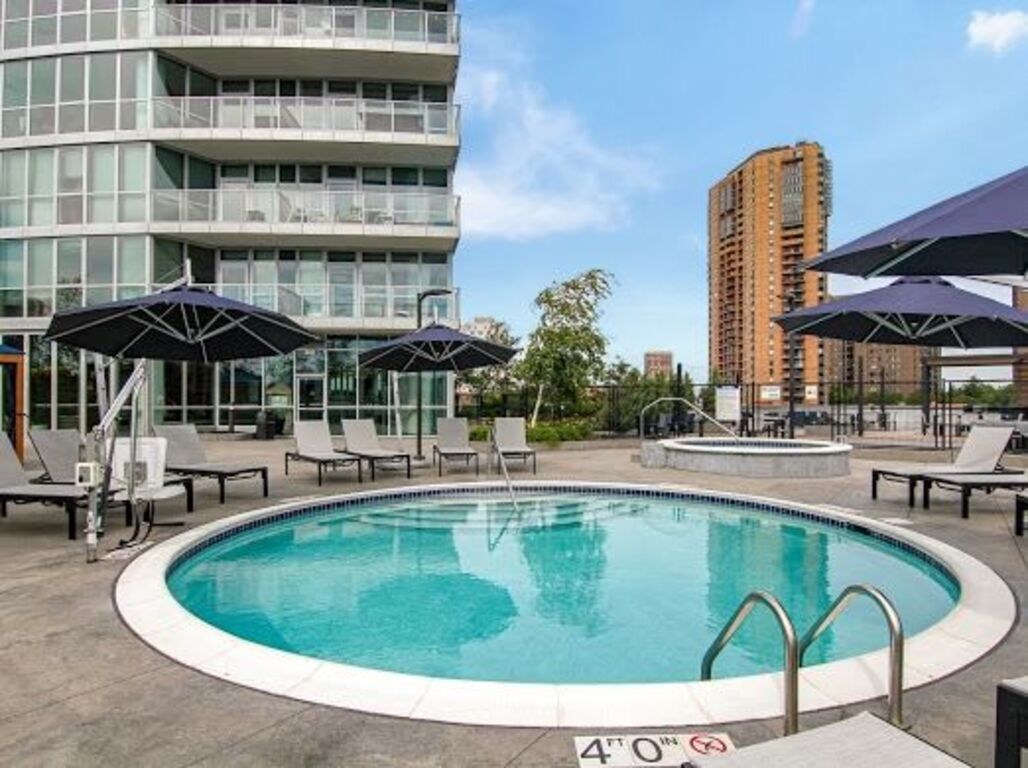 A large swimming pool surrounded by chairs and umbrellas in front of a building.