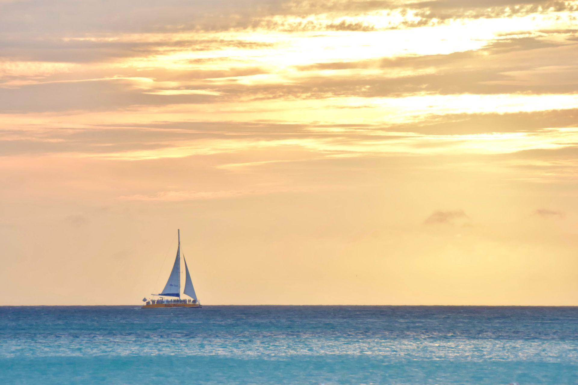 A sailboat in the middle of the ocean at sunset