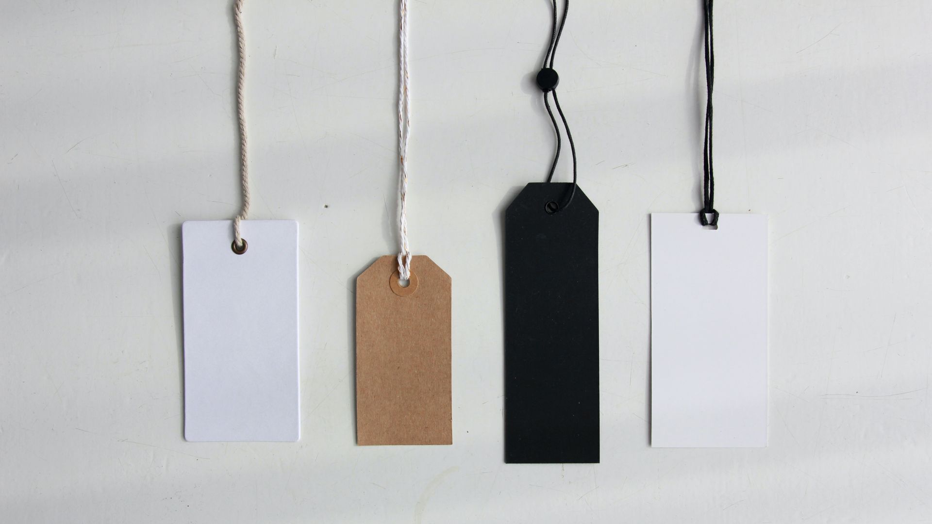 A group of tags hanging from strings on a white surface.