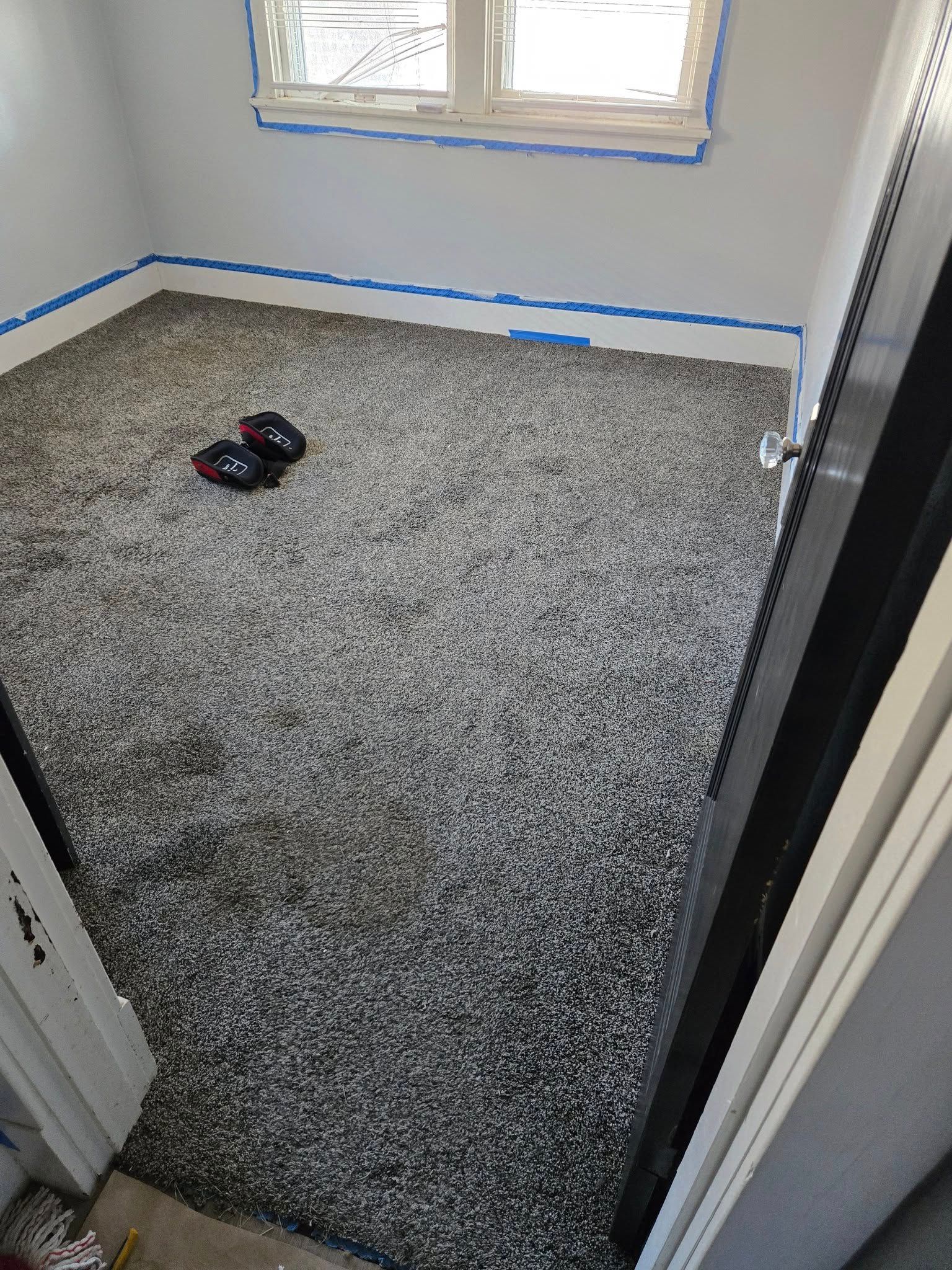 Room with gray and white speckled carpet, blue tape at the base of the walls. Doorway visible.