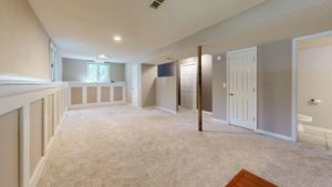 Spacious finished basement with light carpet, neutral walls, white trim, and a wooden support beam.