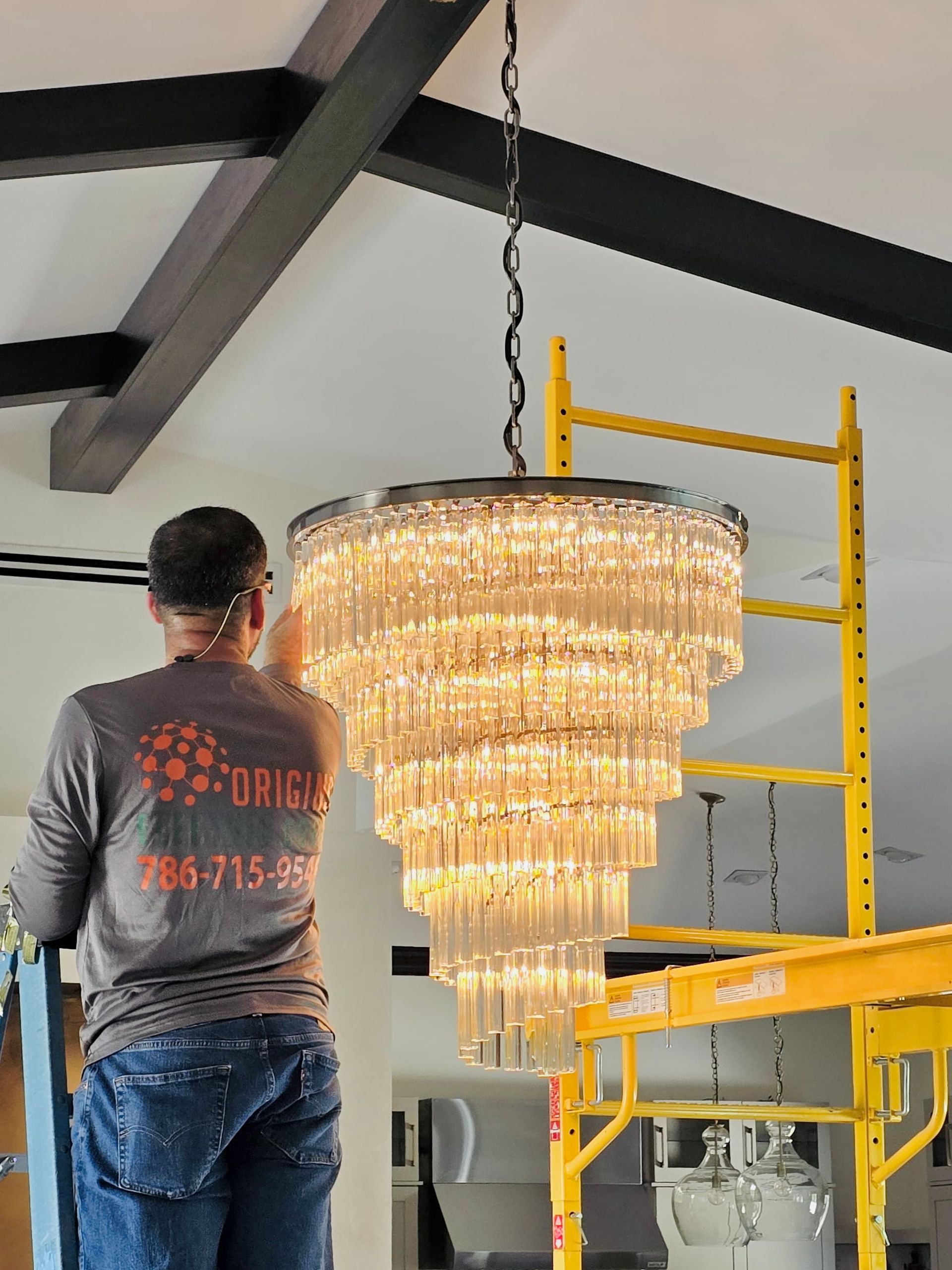 Worker on a yellow scaffold installing a large crystal chandelier indoors
