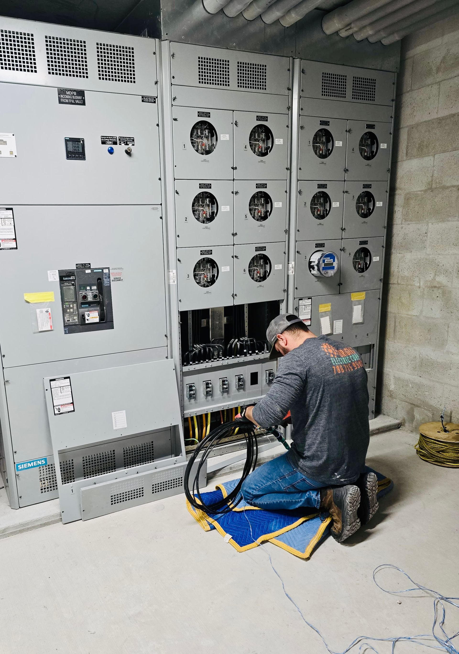 Technician inspecting electrical panel while another works on wiring in a utility room