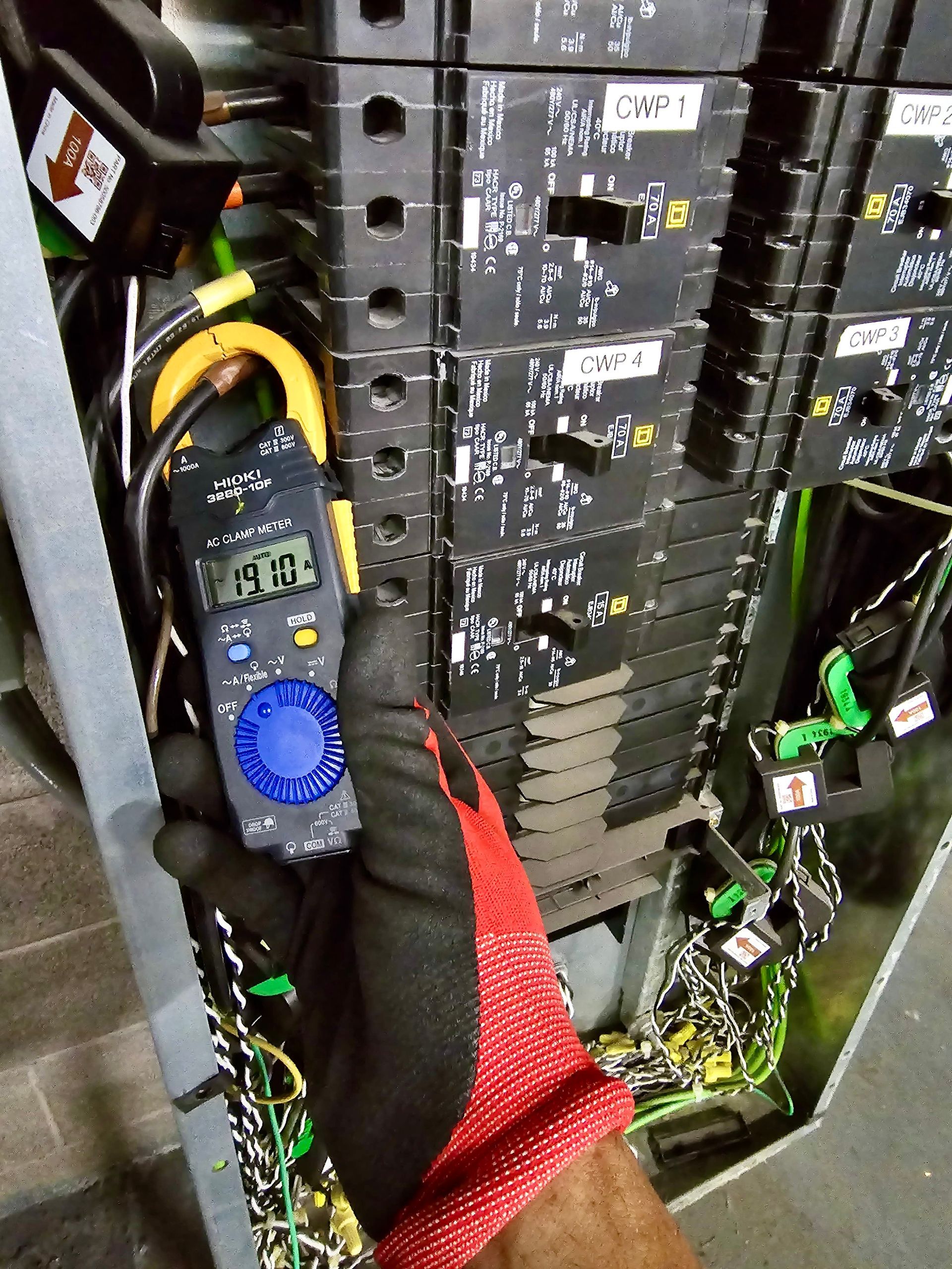 Two workers servicing electrical panels in a utility room, with cables and tools on the floor.
