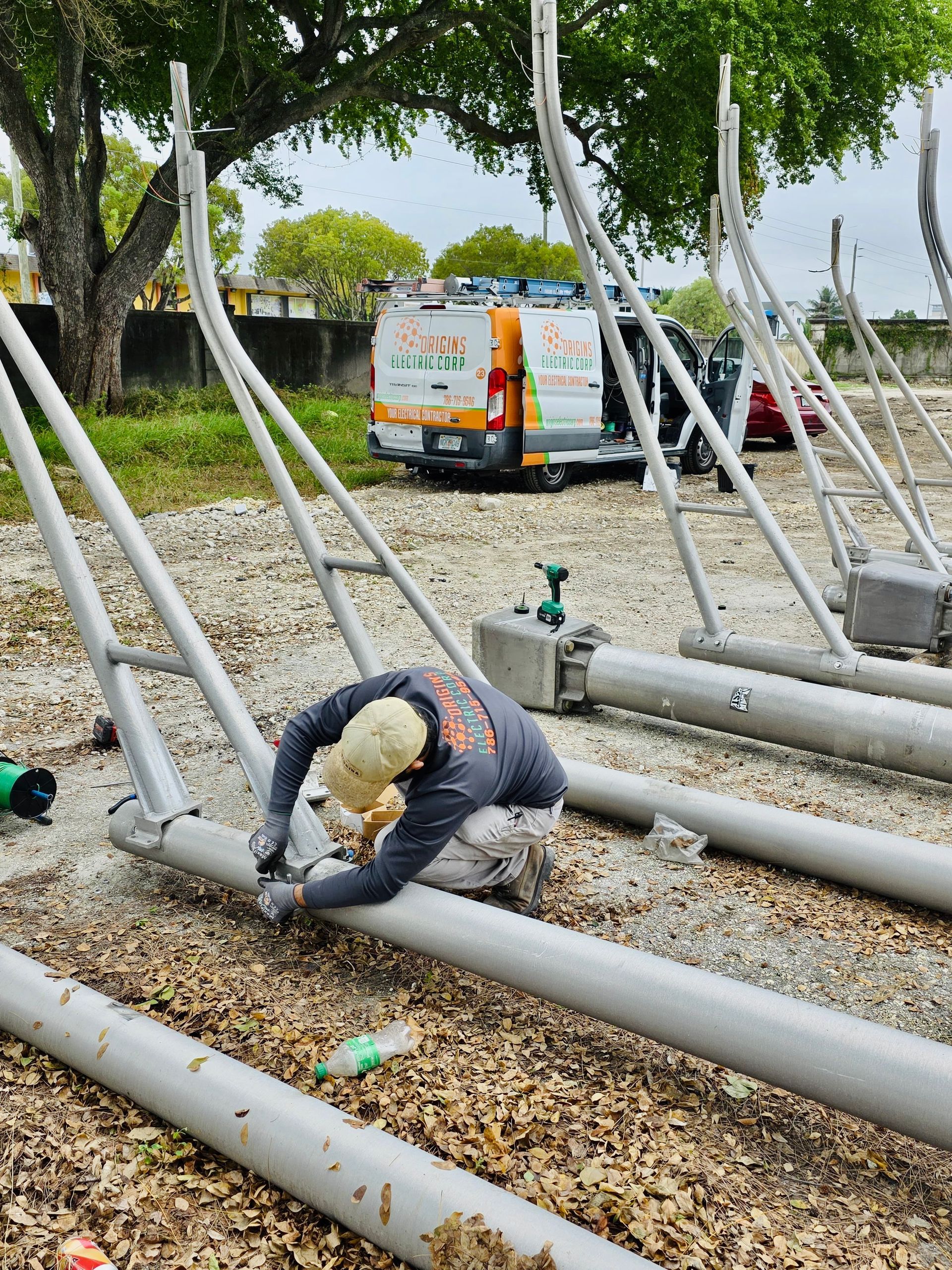 Worker crouching among large white pipes in a gravel area, with a van and trees in the background.