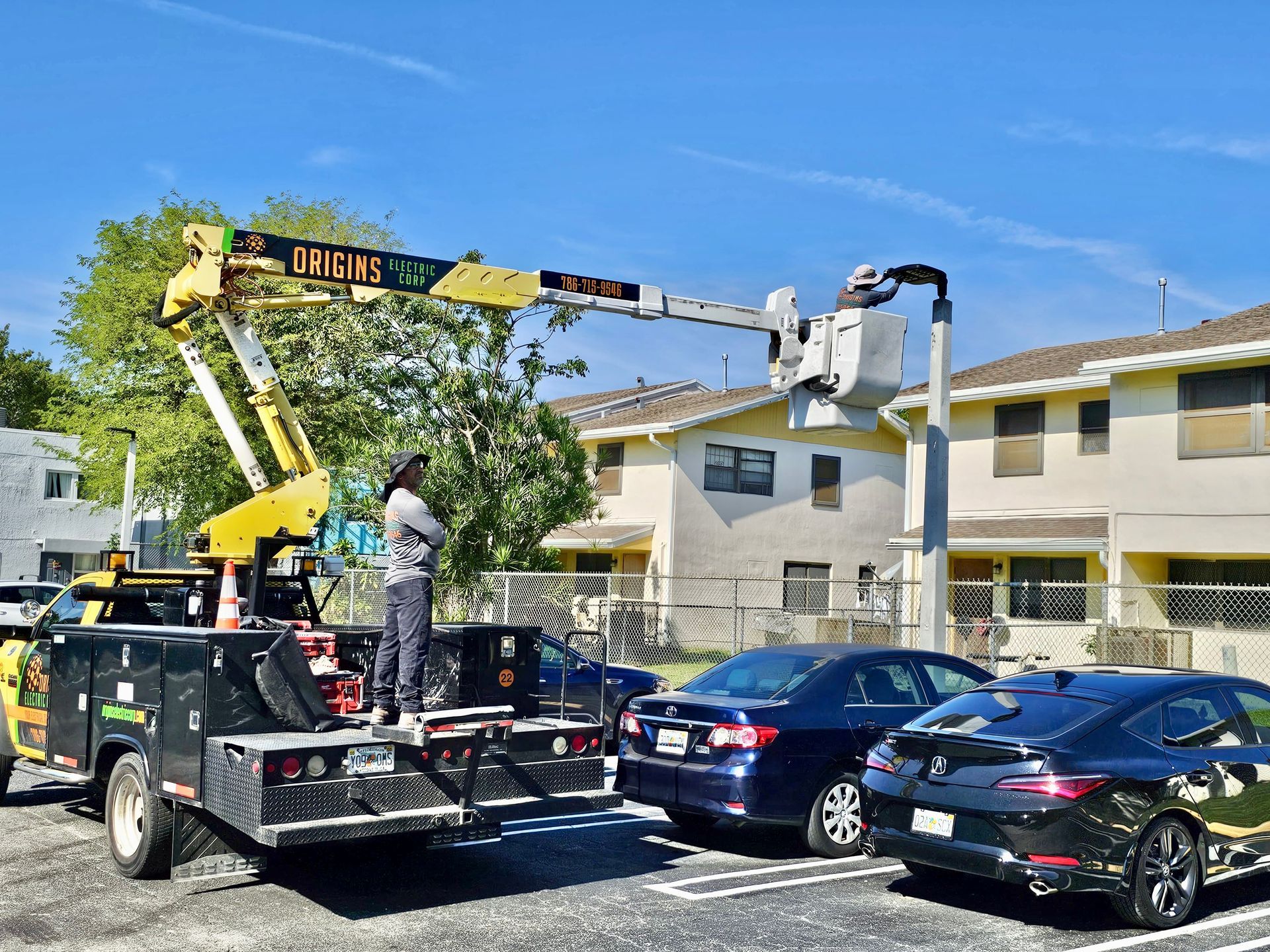Tow truck using crane to lift a car in a residential parking lot with blue cars and apartment buildings nearby