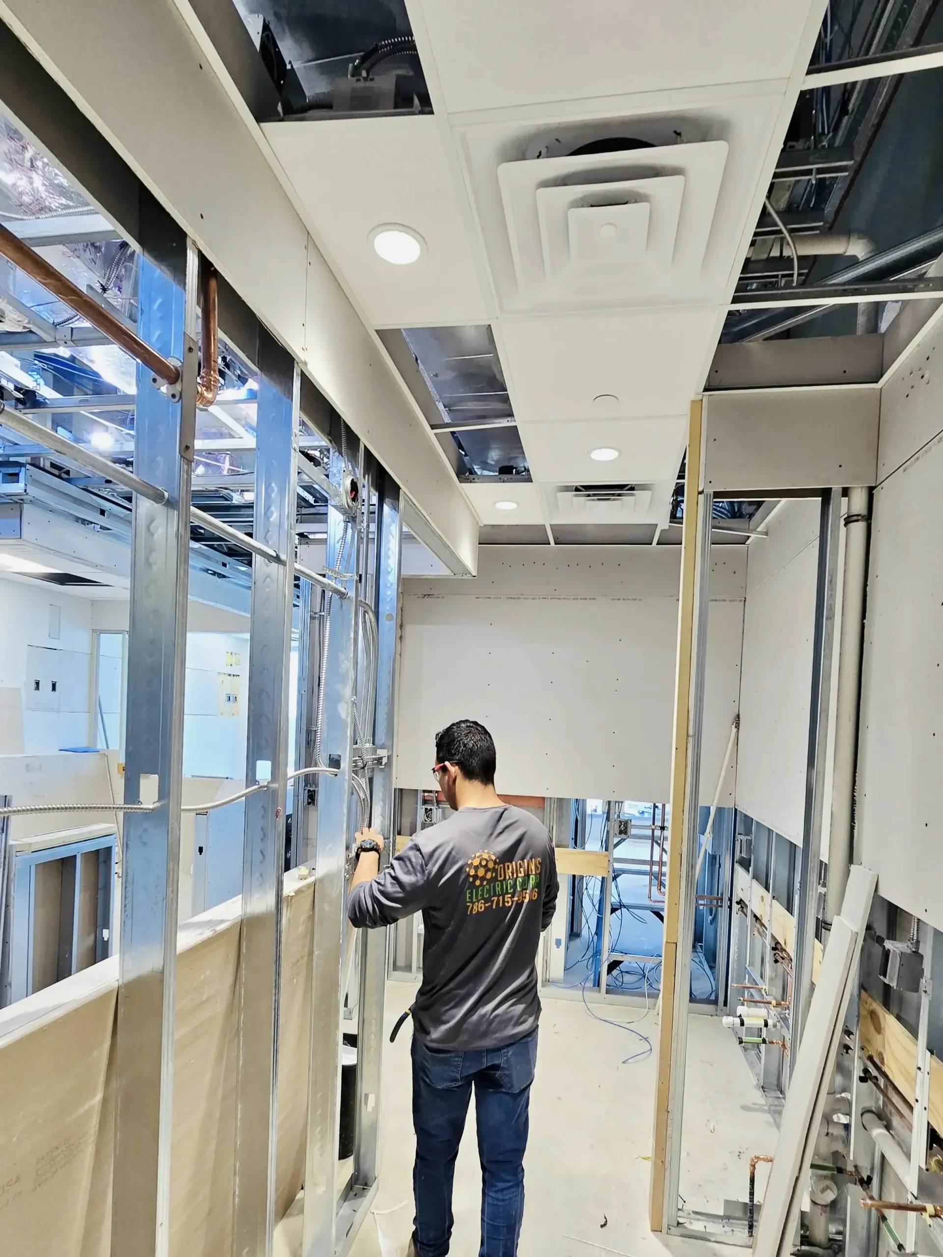 Worker installing drywall and ceiling panels in an unfinished building corridor.