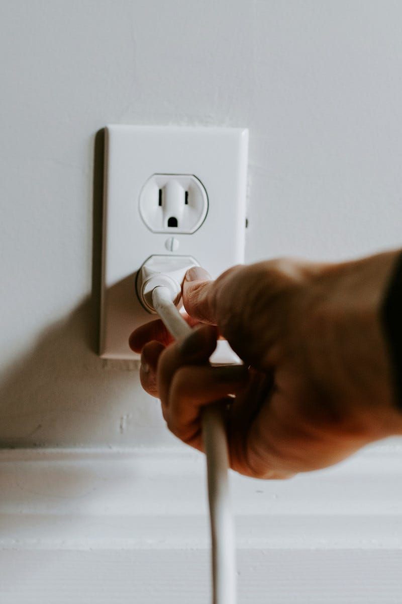 Hand plugging a white cord into a white wall outlet