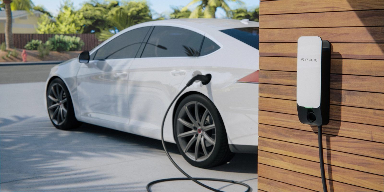 White electric car parked beside a wall-mounted EV charger in a sunny driveway.