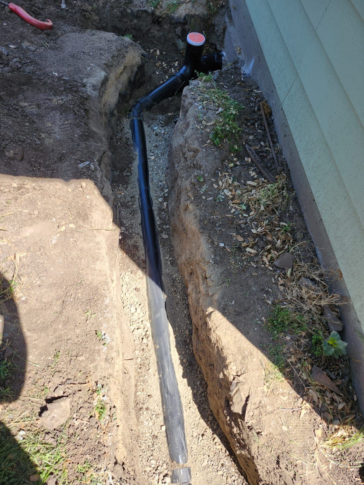 A pipe is being installed in a trench next to a house.