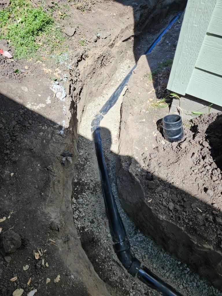 A black pipe is coming out of a hole in the ground next to a house.