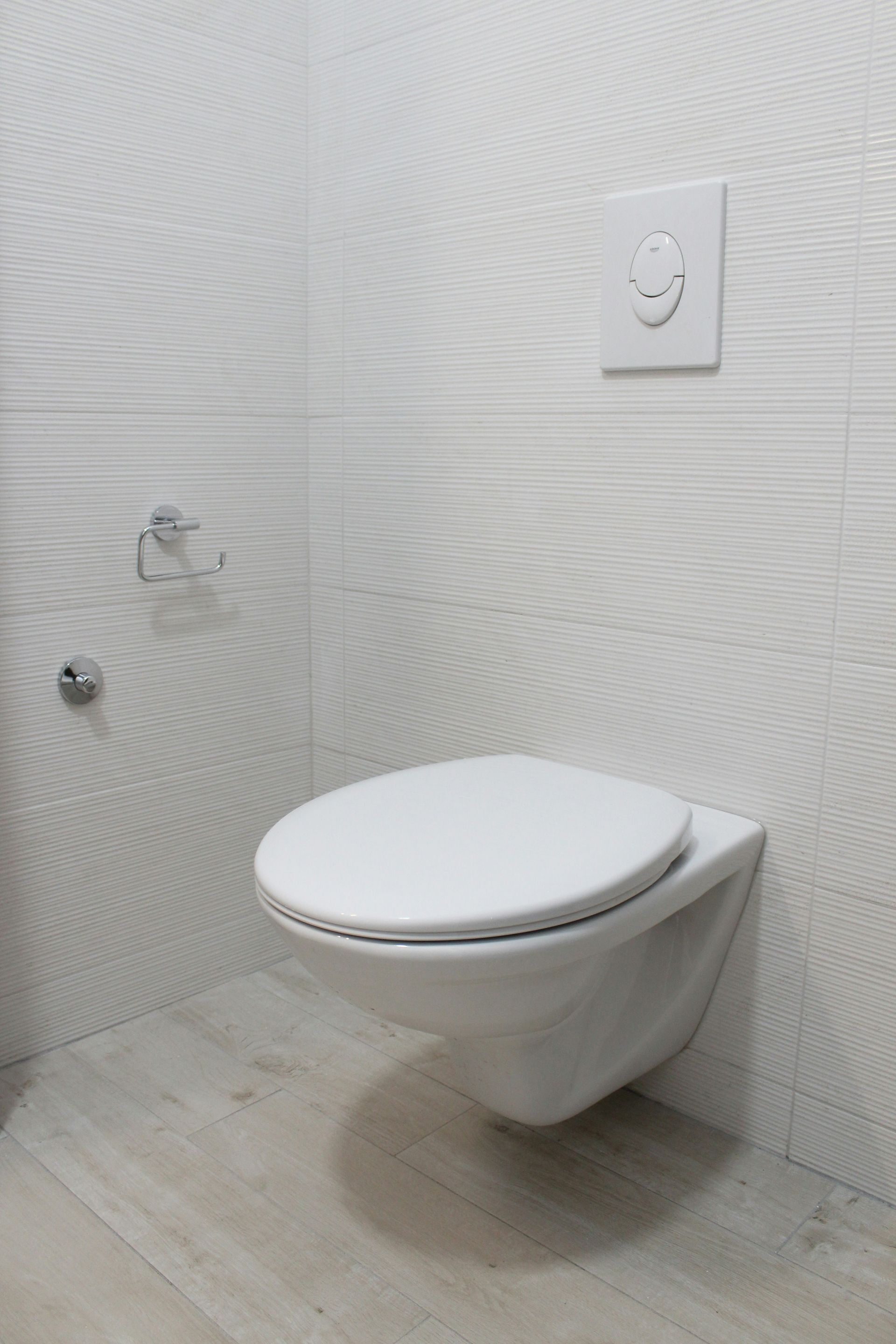 Wit wandtoilet in een moderne badkamer met witte tegelwanden en een spoelknop.
