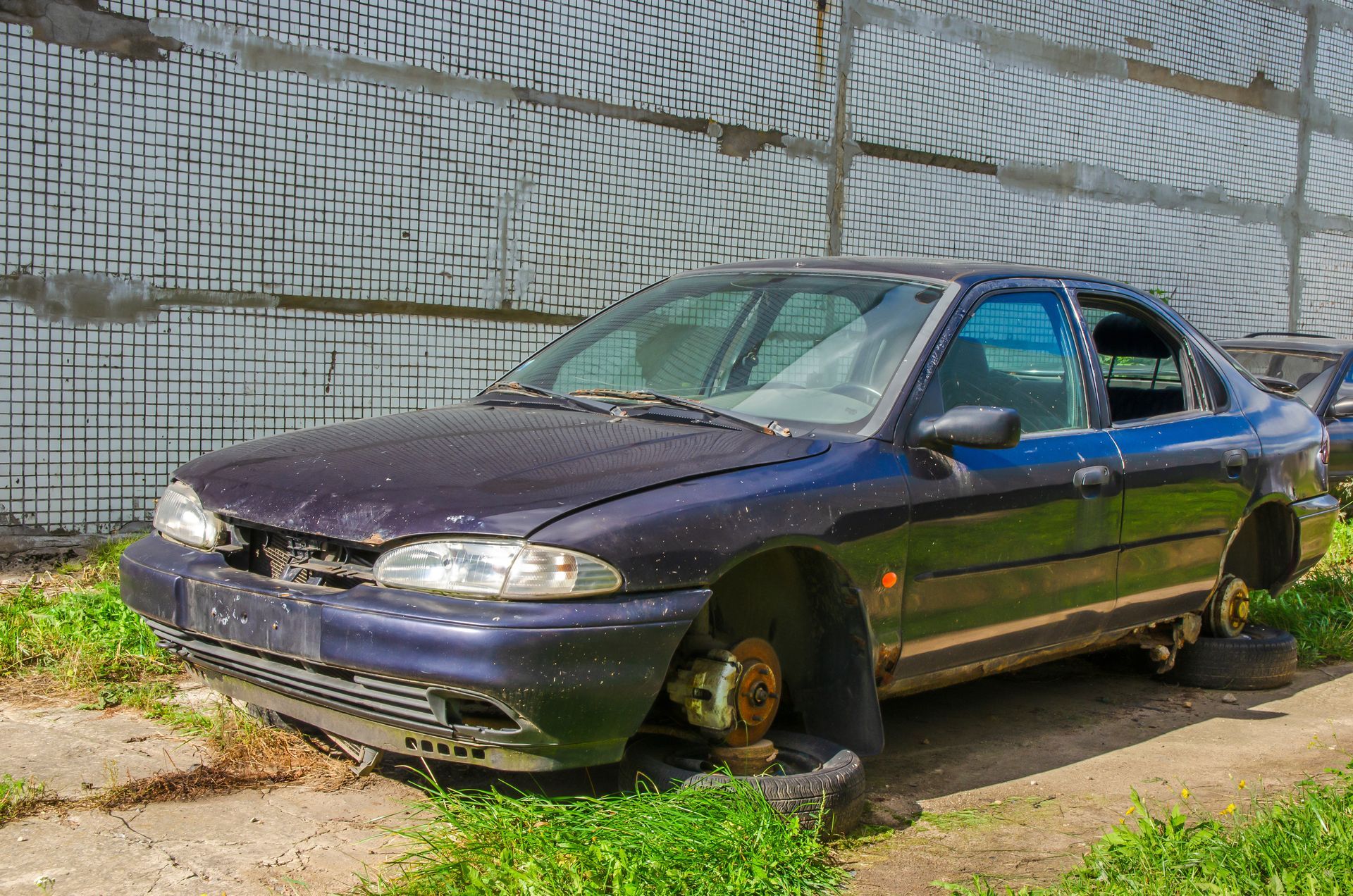Dark blue sedan with missing wheels and faded paint, ready to sell as a junk car
