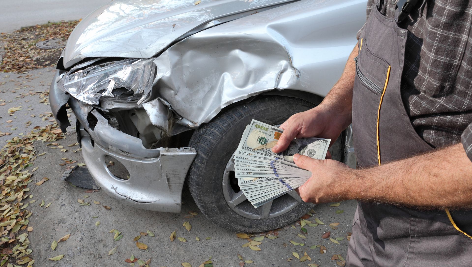 Person holding cash beside a car with a damaged front bumper and dented fender.